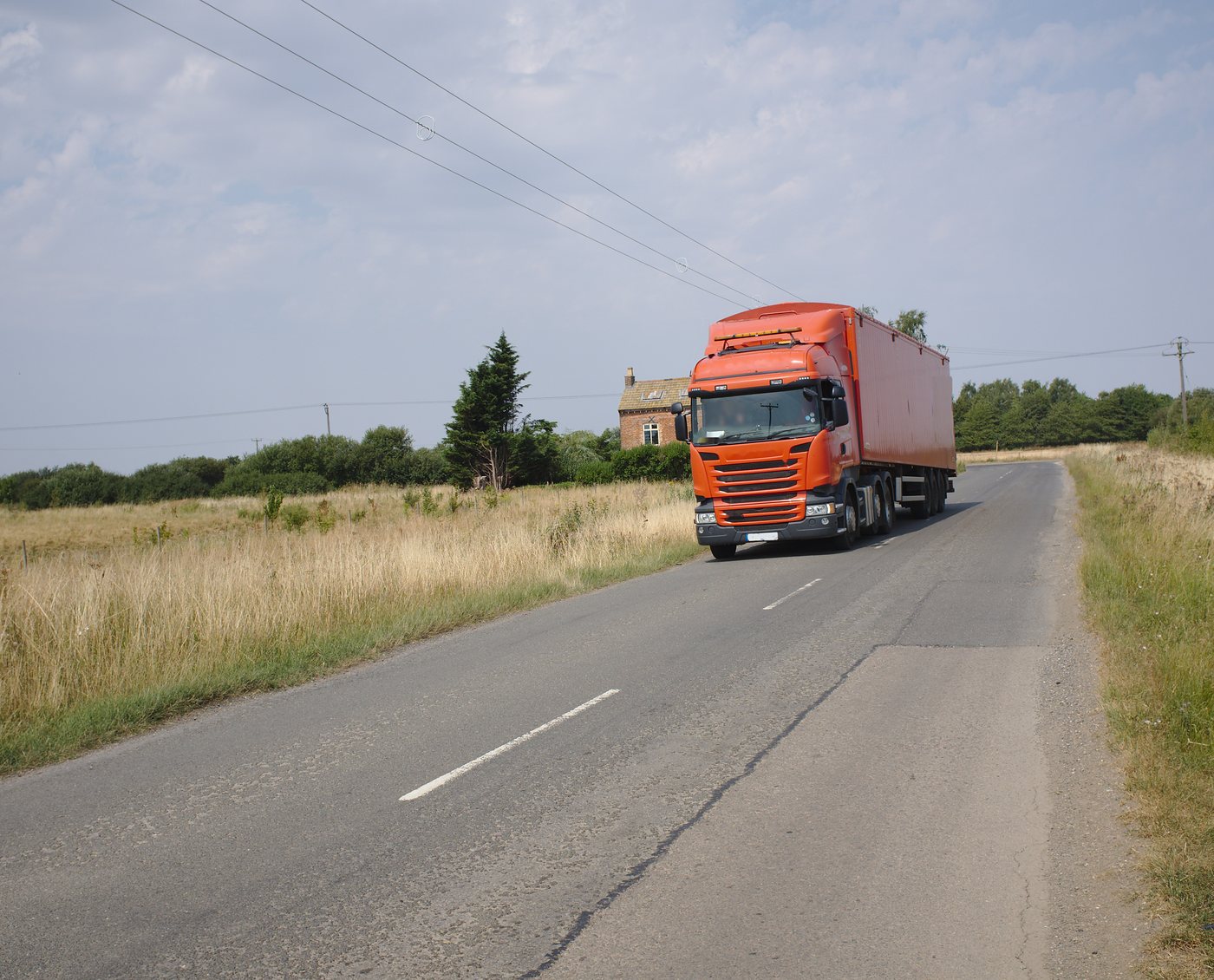 An articulated lorry with a plain trailer coming along a quiet country road between summer fields